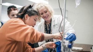 Nursing student assisted during iv set up by instructor in lab coat