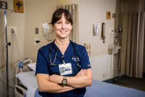 Confident nursing student in blue scrubs smiling in a clinic room
