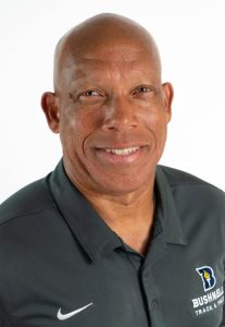 Headshot of a smiling Bushnell University track and field coach wearing a dark team polo shirt.