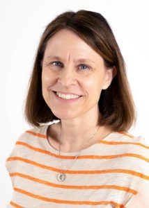 Portrait of a smiling woman with shoulder-length brown hair wearing a cream-colored shirt with orange stripes against a light background.