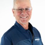 Headshot of a smiling Bushnell University golf coach in a blue team jacket and glasses.