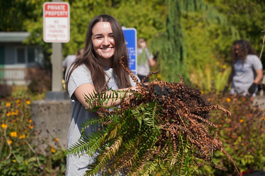 female student smiling at camera while doing yard work