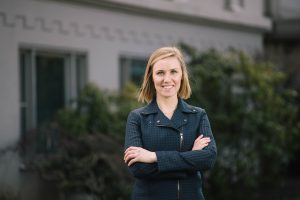 Confident professional woman smiling with a building and trees behind her