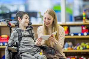 Special education teacher providing reading assistance to child requiring accessibility help