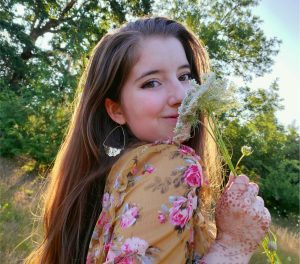 Female student headshot with with a forest background while smelling flowers