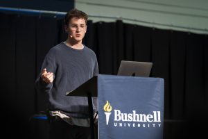 Male student preaches at a podium with their laptop
