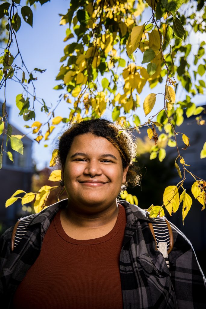 Bushnell University student smiles outdoors beneath colorful autumn leaves on campus.