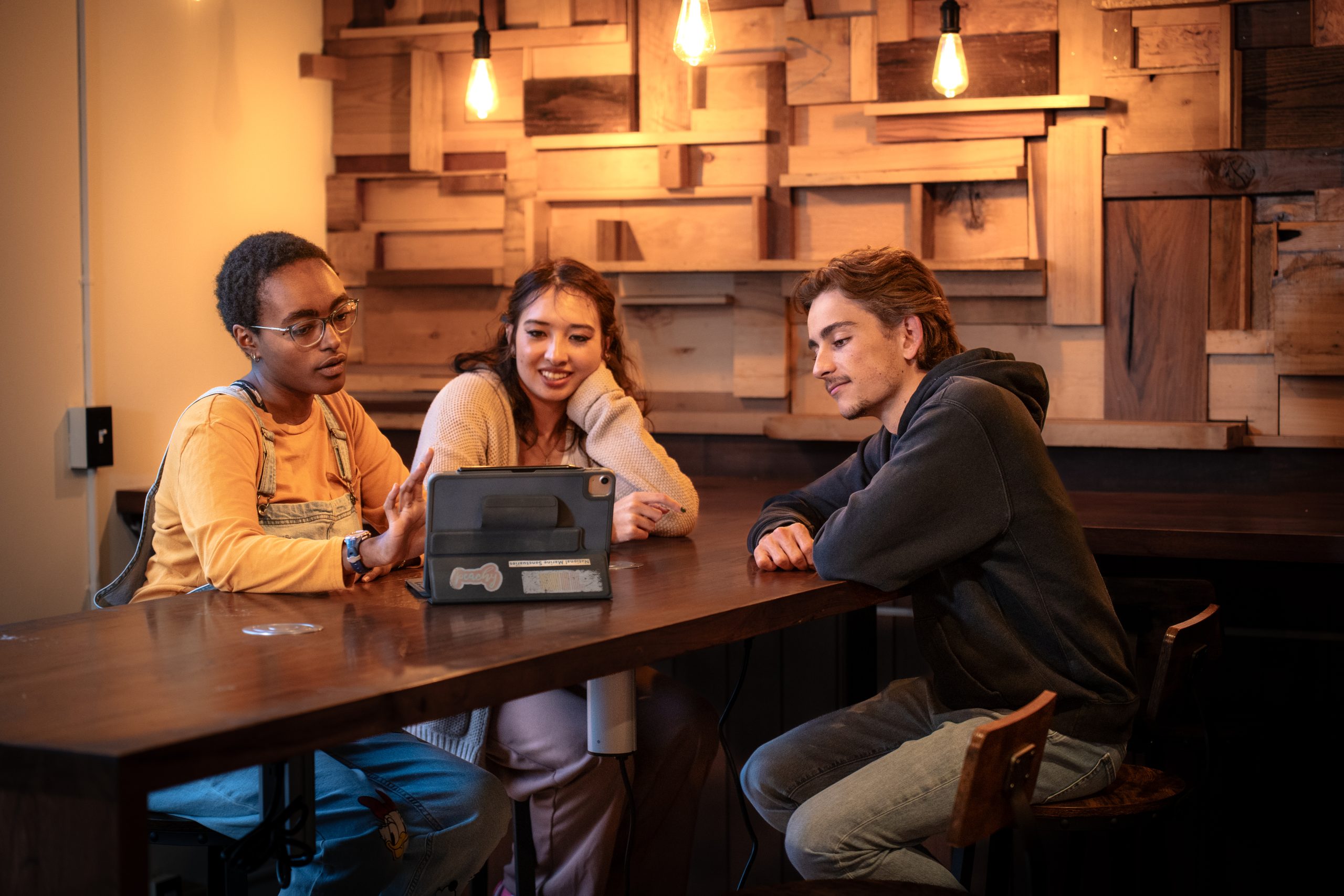 Three Bushnell University students collaborate around a tablet while discussing coursework in a campus study space.