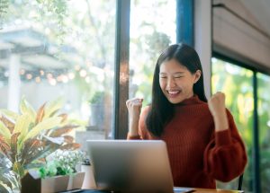 Prospective college student celebrating while viewing admissions or financial aid information on a laptop.