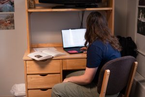 Bushnell University student studies at a desk in a residence hall room using a laptop and textbook.